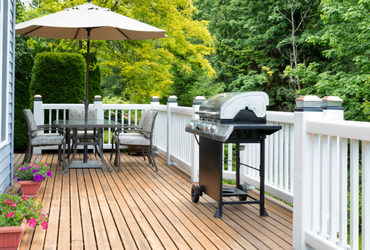 A patio with an umbrella and grill on the back deck.